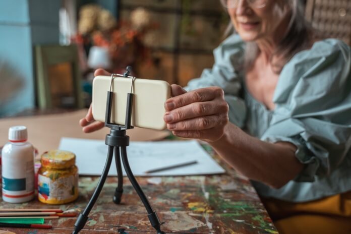 Een oudere dame die volgt een voordelige online kunstles op een smartphone in een houder